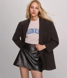 Model wearing a dark blazer over a pink graphic t-shirt and black miniskirt against a pale grey seamless background.