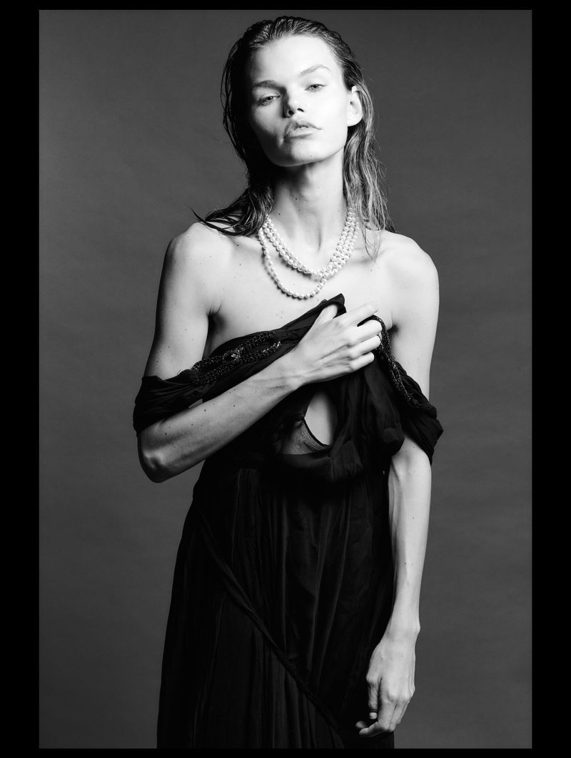 Model Daphne Maas wearing a dark gown and pearl necklace against a grey studio backdrop in a portrait by Oscar Ozbay.