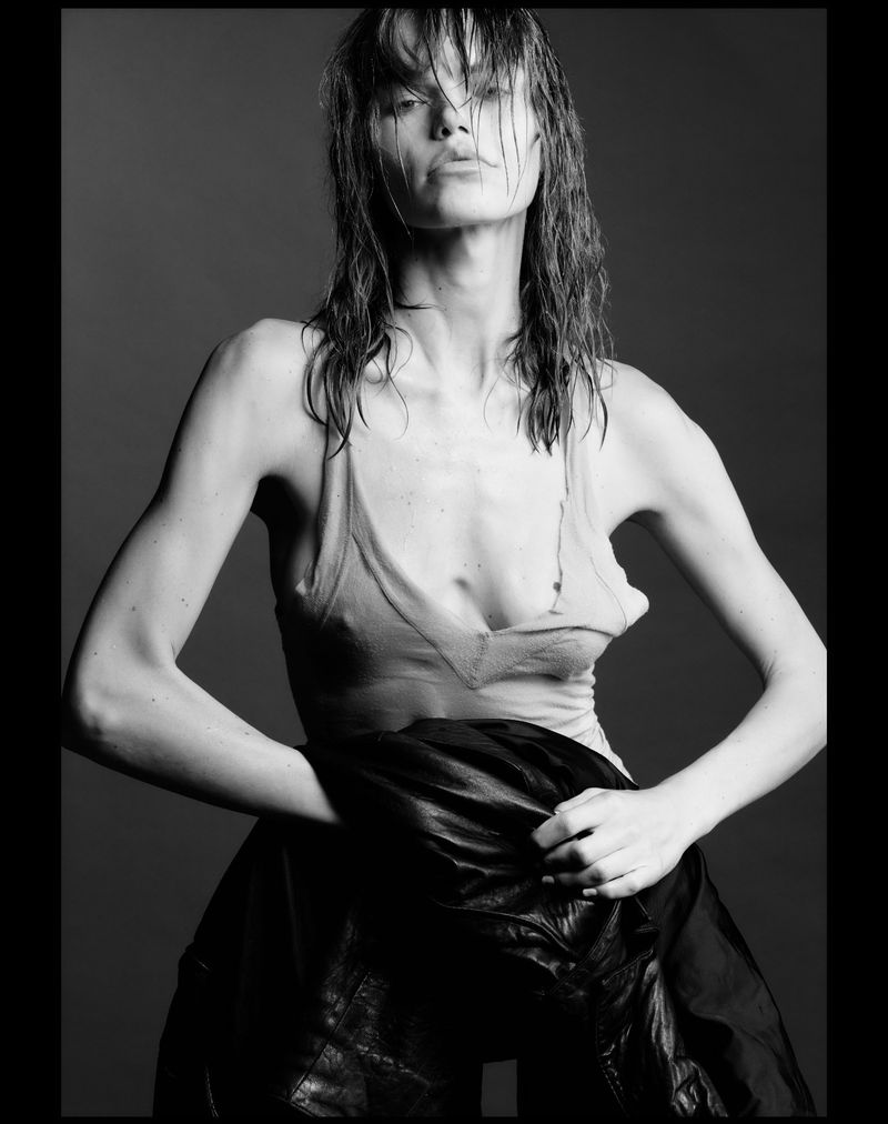 Monochrome portrait of model Daphne Maas with wet hair wearing a light tank top and holding a dark jacket against a grey studio backdrop