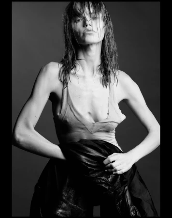 Monochrome portrait of model Daphne Maas with wet hair wearing a light tank top and holding a dark jacket against a grey studio backdrop