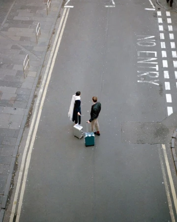 High angle view of a stylish couple standing on a city street with their suitcases, ready for a trip, under soft, natural light.