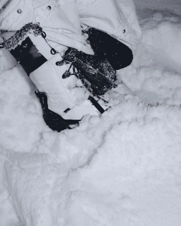 Close-up on person wearing white snow boots and black gloves, surrounded by fresh snow. Focus on footwear, apparel, and winter setting.