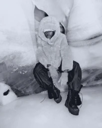 Model wearing a hooded winter coat and heavy boots seated within a snowy glacial crevasse for Ugg