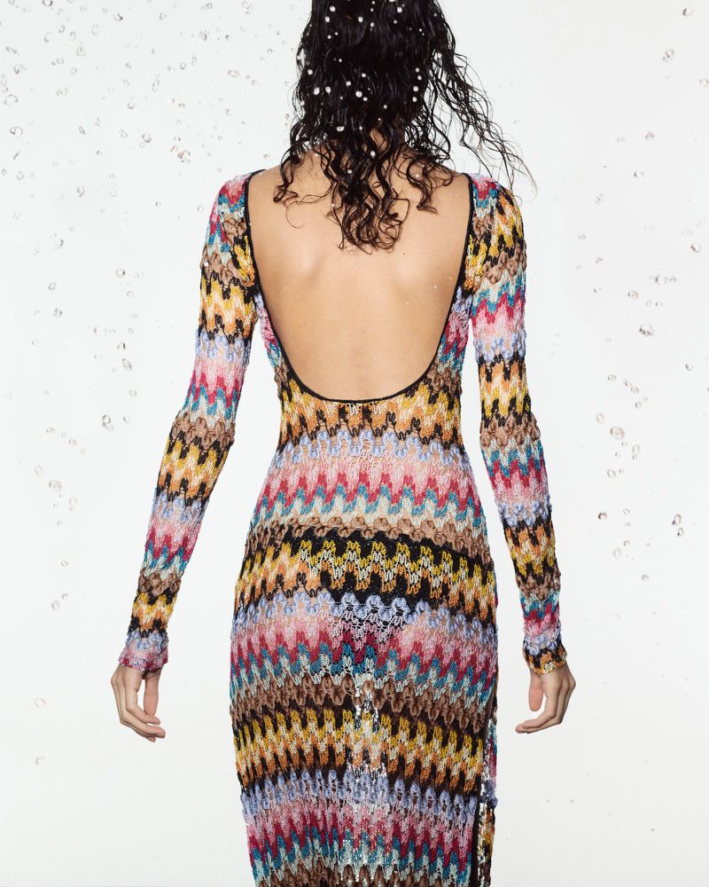 Back view of a woman with water pearls in her hair wearing a colorful knit dress with a low back and long sleeves in studio setting.