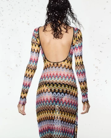Back view of a woman with water pearls in her hair wearing a colorful knit dress with a low back and long sleeves in studio setting.