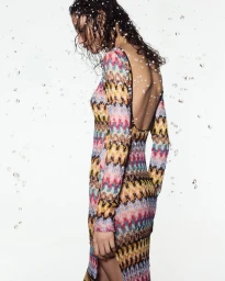 Model in a colourful patterned knit dress against a white background with floating water droplets