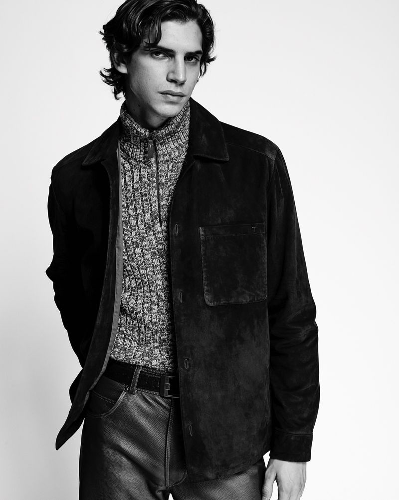 Black and white studio portrait of a young adult male wearing a textured sweater, dark suede shirt-jacket, dark pants, and a belt.