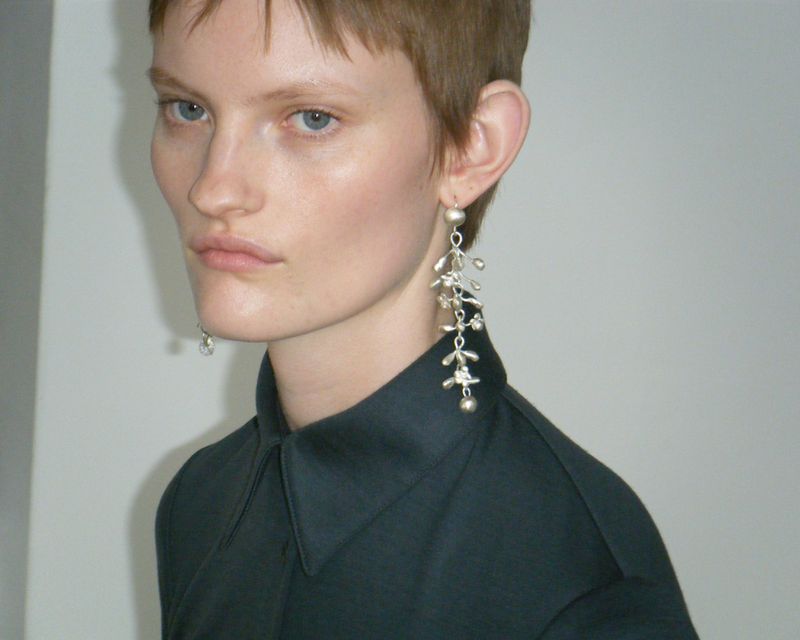 Headshot of a fair-skinned young woman with short brown hair wearing a dark collared shirt and ornamental silver earrings.