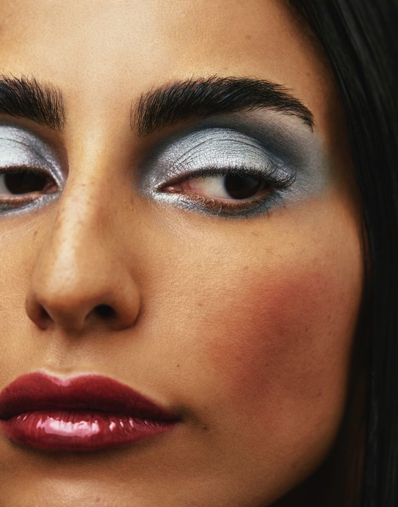 Close-up of a woman's face, emphasizing silver and gray eyeshadow, dark eyeliner, glossy lips, and dark eyebrows.