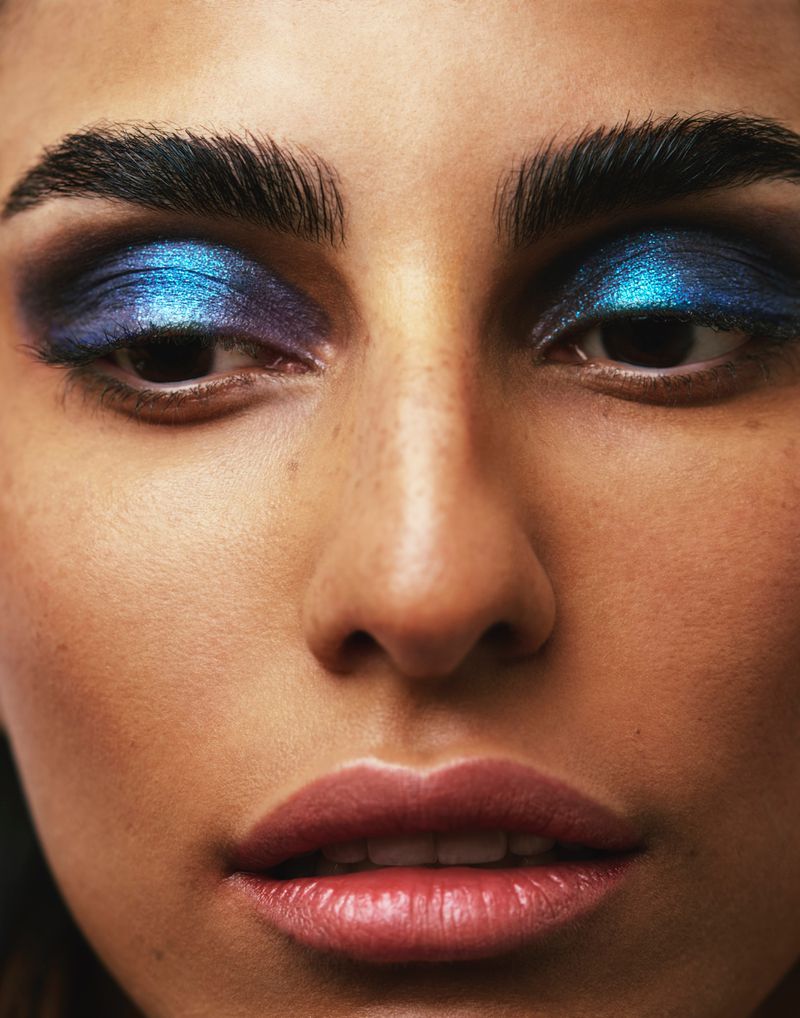Close-up portrait of a woman with dramatic blue and purple eye makeup, showcasing beauty and cosmetic artistry.