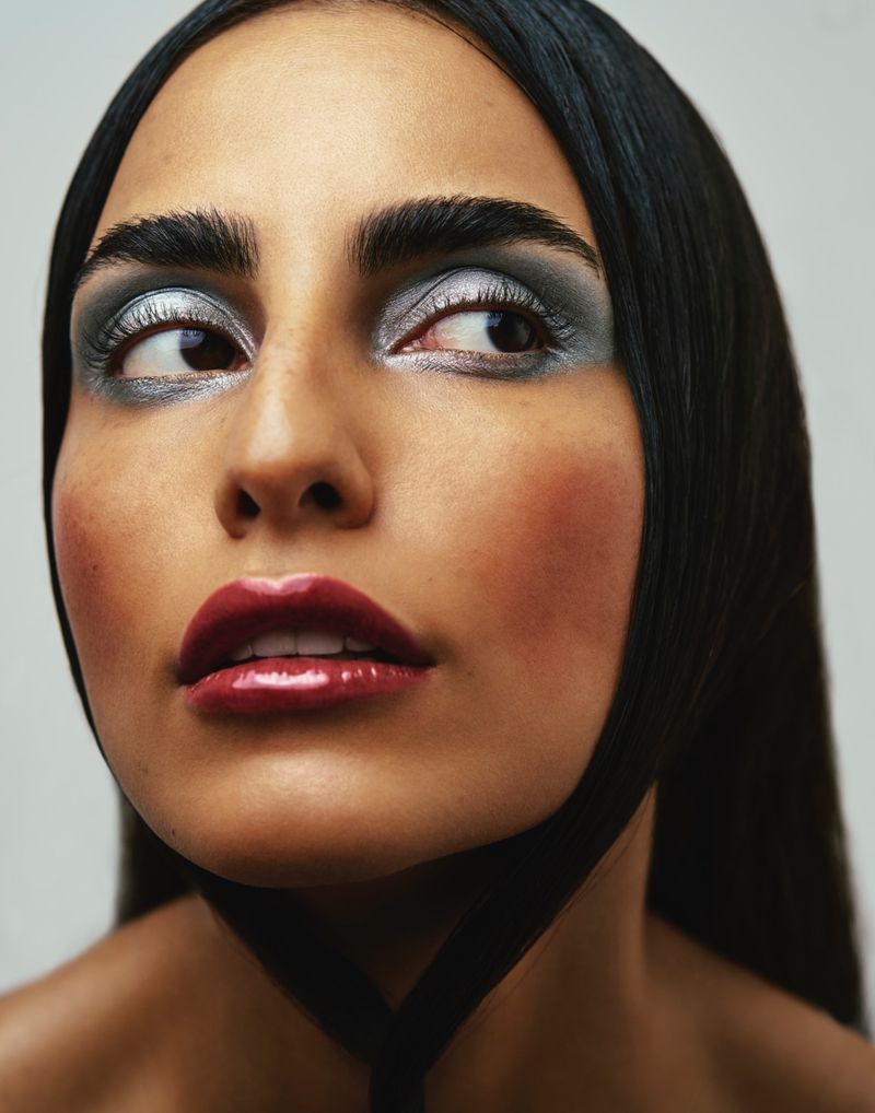 Close-up beauty portrait of a woman with metallic silver eyeshadow, dark brows, and glossy burgundy lips against a pale background