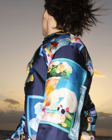 Person wearing a blue silk shirt with baroque print against an evening sky