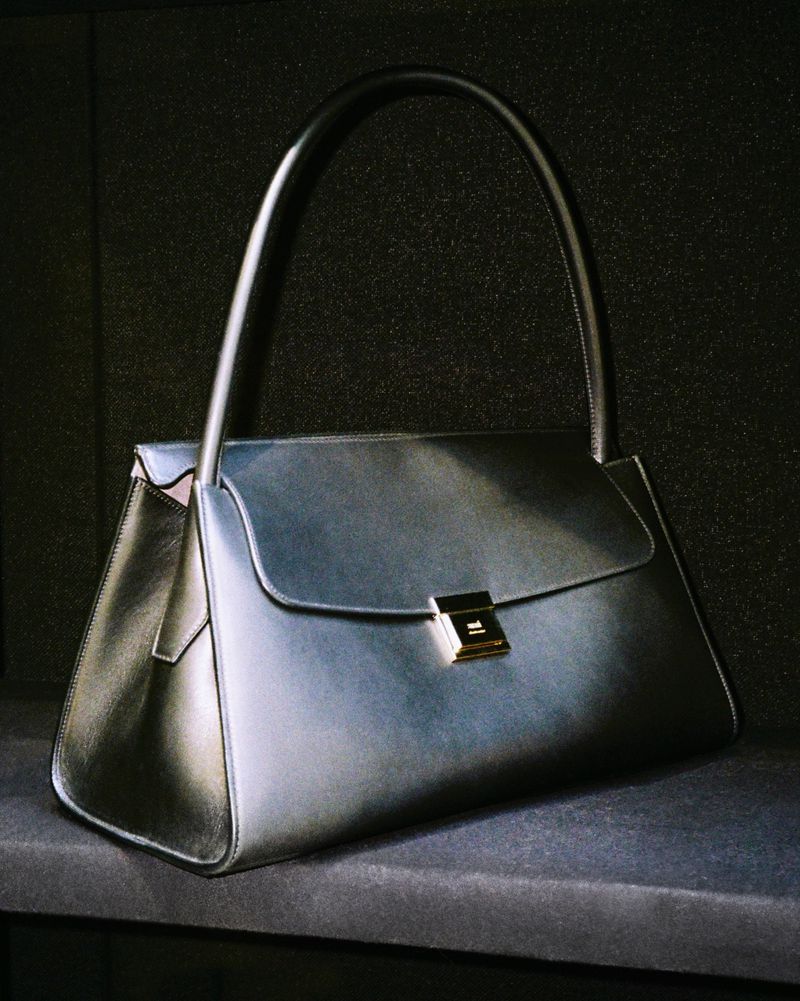 Elegant black leather handbag with a gold clasp on a dark surface, capturing a fashion-forward style and minimalist design.