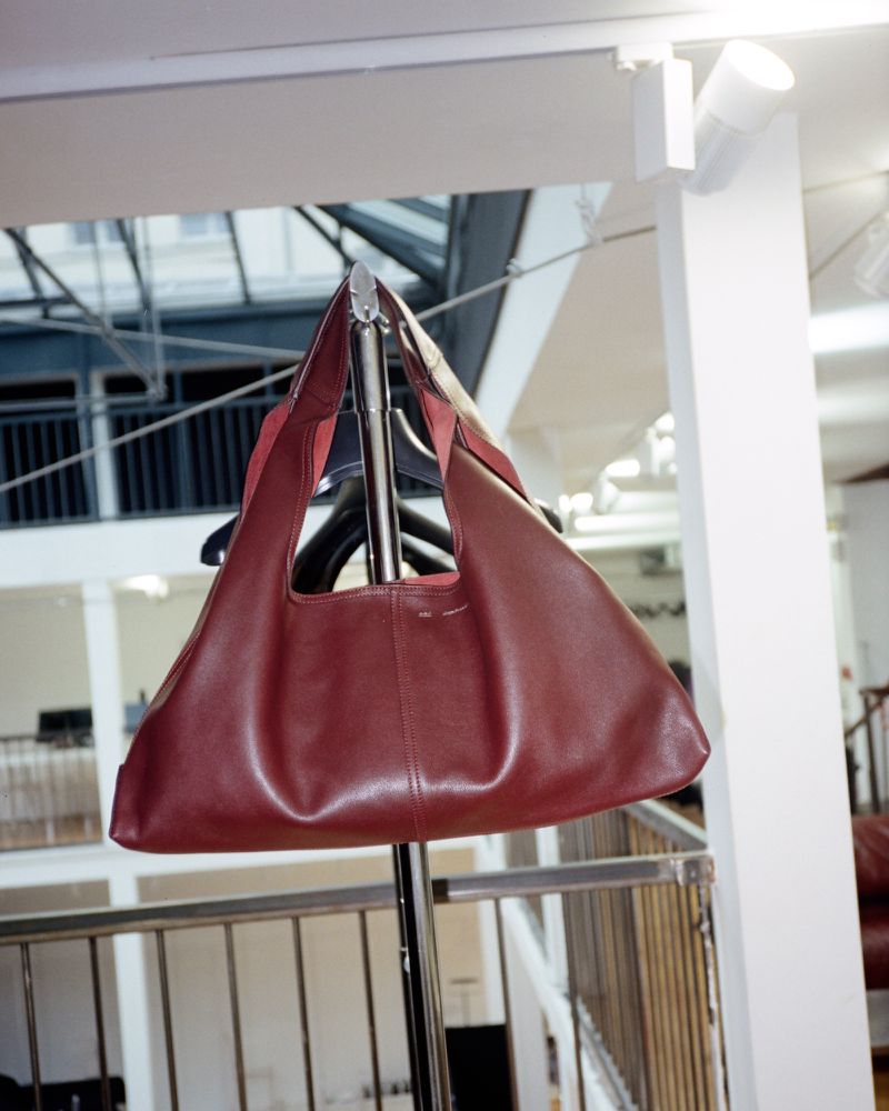 Burgundy leather hobo bag hanging on a metal rack with interior atrium background. Modern, stylish women's handbag for fashion accessory.