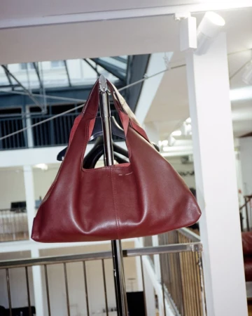 Burgundy leather hobo bag hanging on a metal rack with interior atrium background. Modern, stylish women's handbag for fashion accessory.