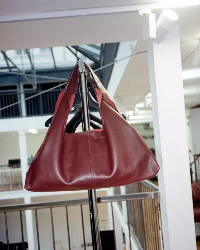Burgundy leather hobo handbag hanging on a metal rack inside a bright showroom interior.
