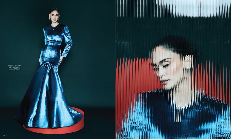 A model poses in a blue satin gown against a dark green background. The shot includes a refraction effect over the model's face.