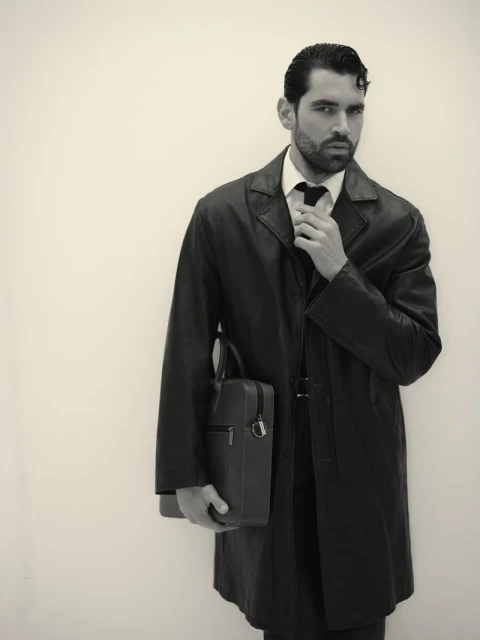 Monochrome portrait of an adult man in an overcoat, adjusting his tie, and holding a briefcase against a plain background.