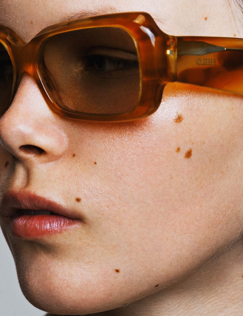 Close-up of a woman's face wearing amber-tinted sunglasses, highlighting the eyewear's style and color against her skin.