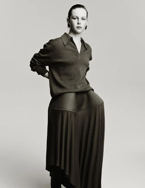 Model Thea Almqvist wearing a collared polo sweater and sculptural pleated wide-leg trousers against a neutral studio backdrop.