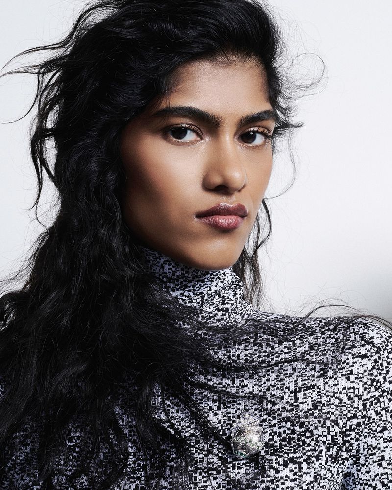 Portrait of an adult female with long, dark hair, wearing a patterned high-neck top in a studio setting with a plain background.