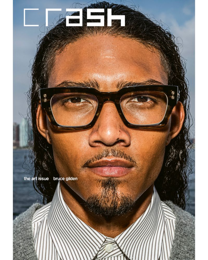 Close-up magazine cover featuring a man with glasses, wearing a striped shirt and grey sweater, with a city skyline in the background.