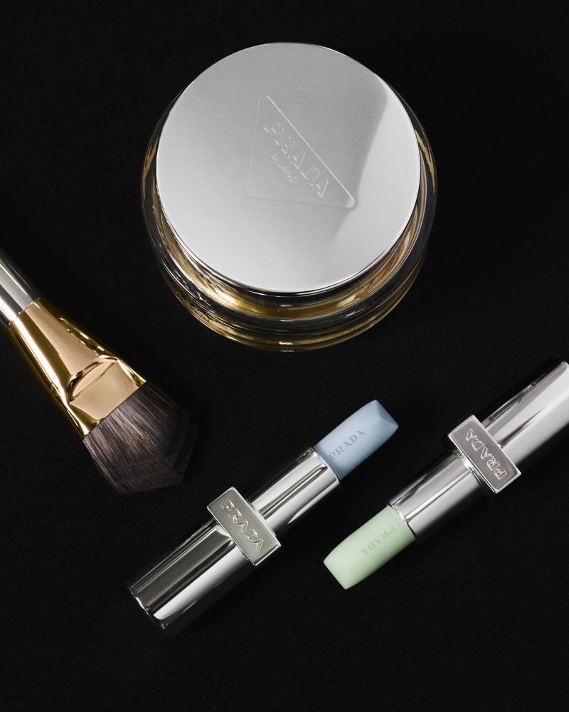 Cosmetic products on a black background featuring a jar with a silver lid, lipsticks, and a makeup brush.