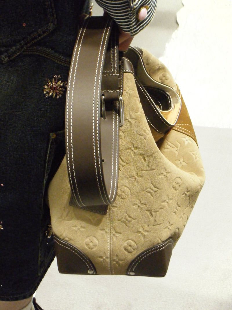 Close-up of a Louis Vuitton hobo bag with a tan patterned body, brown leather accents, and an adjustable shoulder strap. Fashion accessory.