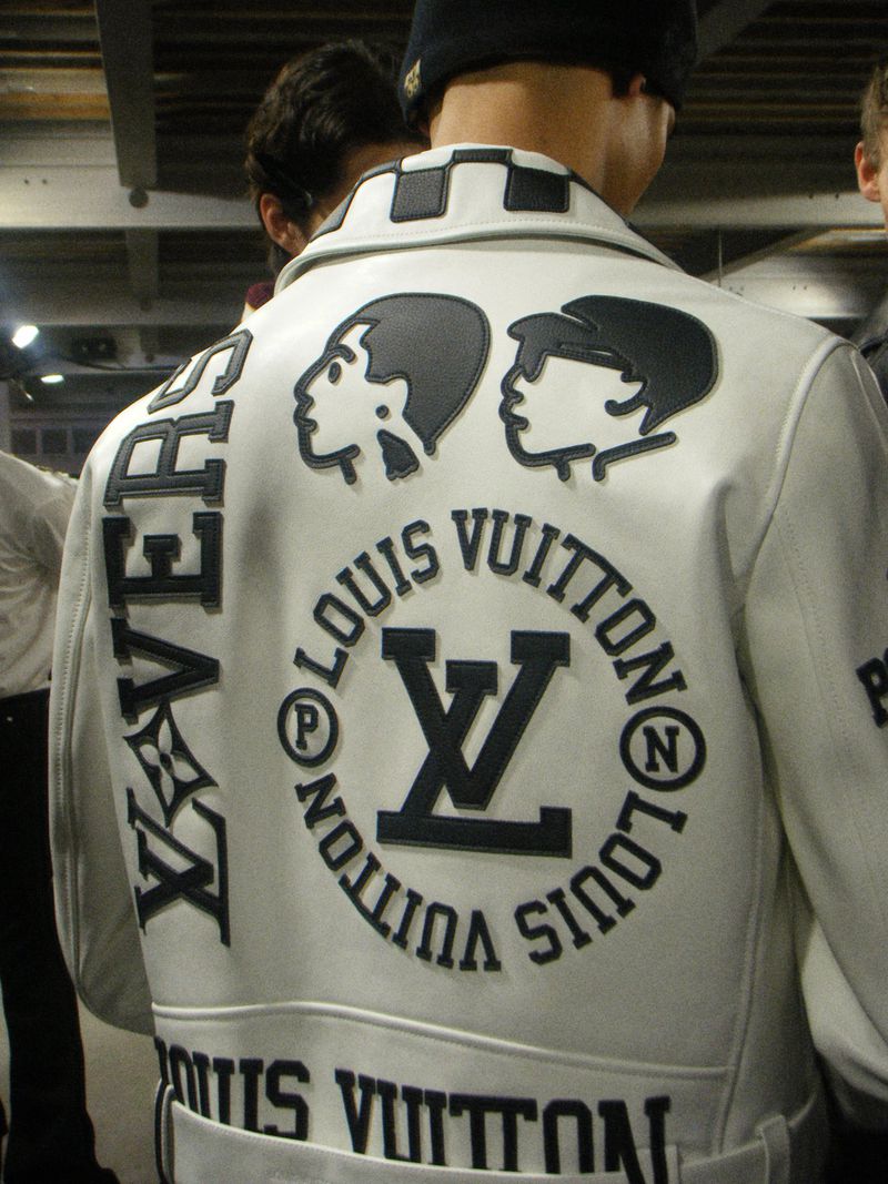 Person wearing a white Louis Vuitton jacket with black graphic designs and text, indoors, showcasing fashion apparel.