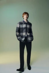 Model Calum Harper wearing a plaid jacket and black trousers against a gradient green background
