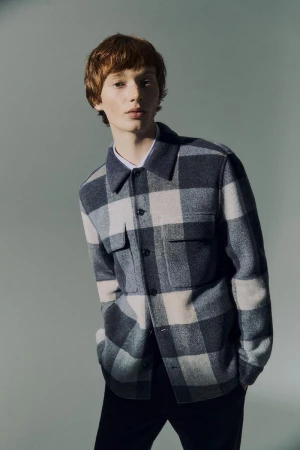 Model Calum Harper wearing a blue and white plaid shirt against a solid grey studio background.
