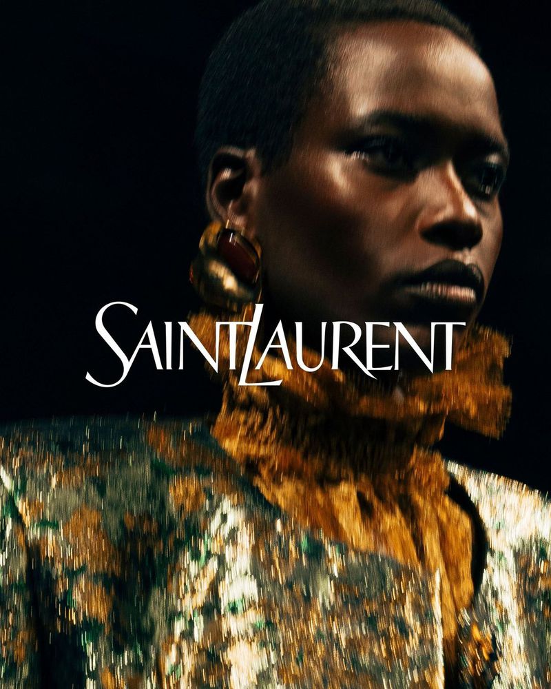 Close-up of Black woman with gold dress and earrings, Saint Laurent logo, dark background. Fashion, beauty, and celebrity visual content.