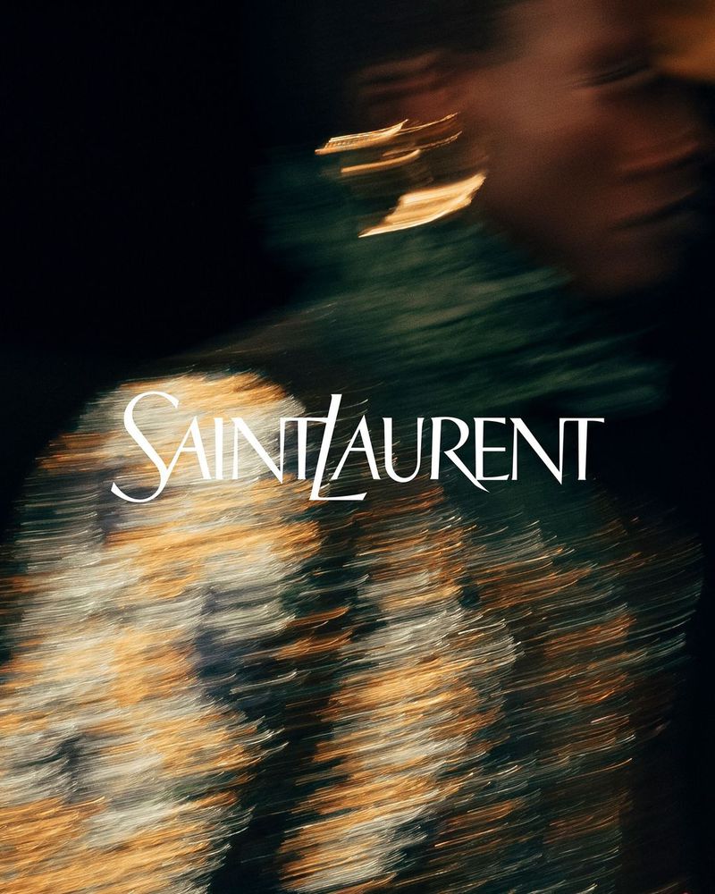 Fashion advertisement featuring a blurry portrait of a person with gold earrings and an abstract top, with Saint Laurent logo overlay.