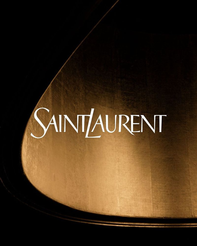 Saint Laurent logo on a dark metallic surface, gold tone, brand promotion, luxury goods, fashion industry advertisement.