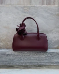 Burgundy leather handbag with flower detail resting on a stone surface