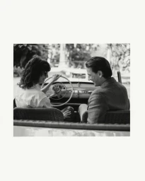 Black and white editorial image of a man and woman seated inside a classic convertible car for Tod's SS25 campaign.