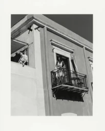 Models standing on balconies of a light-colored stucco building in a black and white fashion campaign photograph