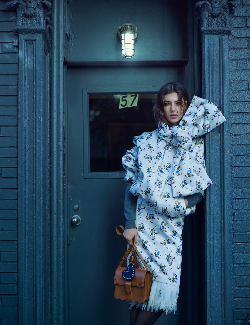 A woman poses in a floral coat dress with a brown handbag against a blue door, creating a street-style fashion portrait with cool tones.