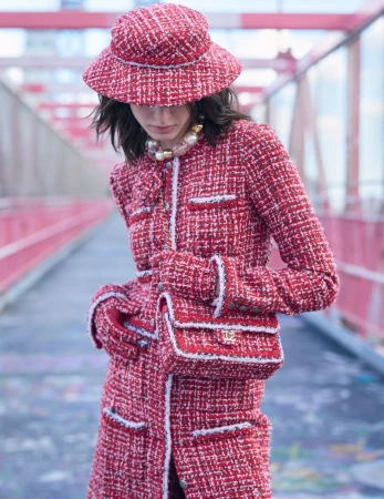 Model in red tweed coat, matching bucket hat, and gloves holding a tweed handbag on a bridge