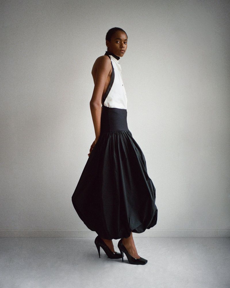 Studio shot of an African American woman wearing a black and white halter top and a voluminous black skirt, striking a pose.