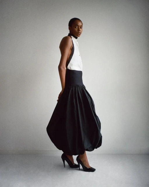 Studio shot of an African American woman wearing a black and white halter top and a voluminous black skirt, striking a pose.