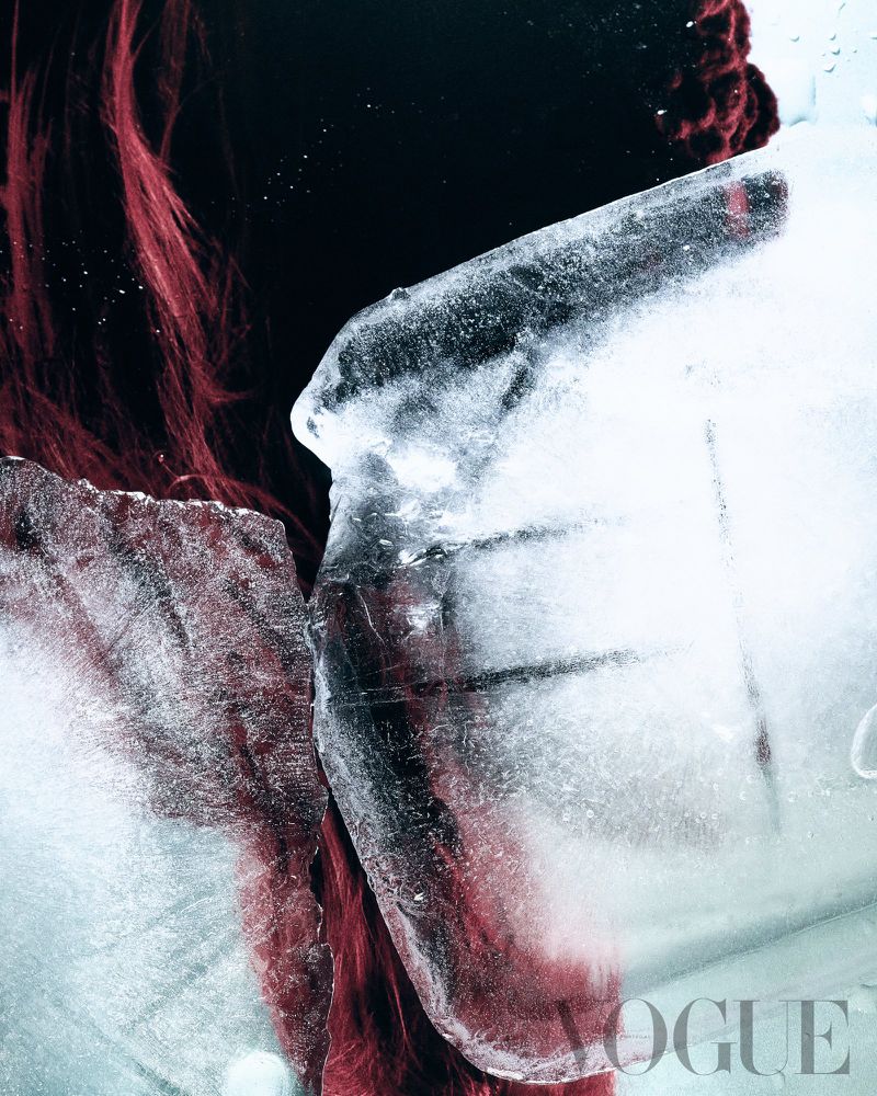 Dramatic conceptual beauty portrait with a woman's face half-obscured by large blocks of textured ice against a stark black backdrop.