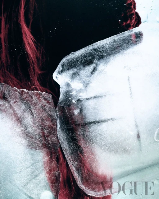 Dramatic conceptual beauty portrait with a woman's face half-obscured by large blocks of textured ice against a stark black backdrop.