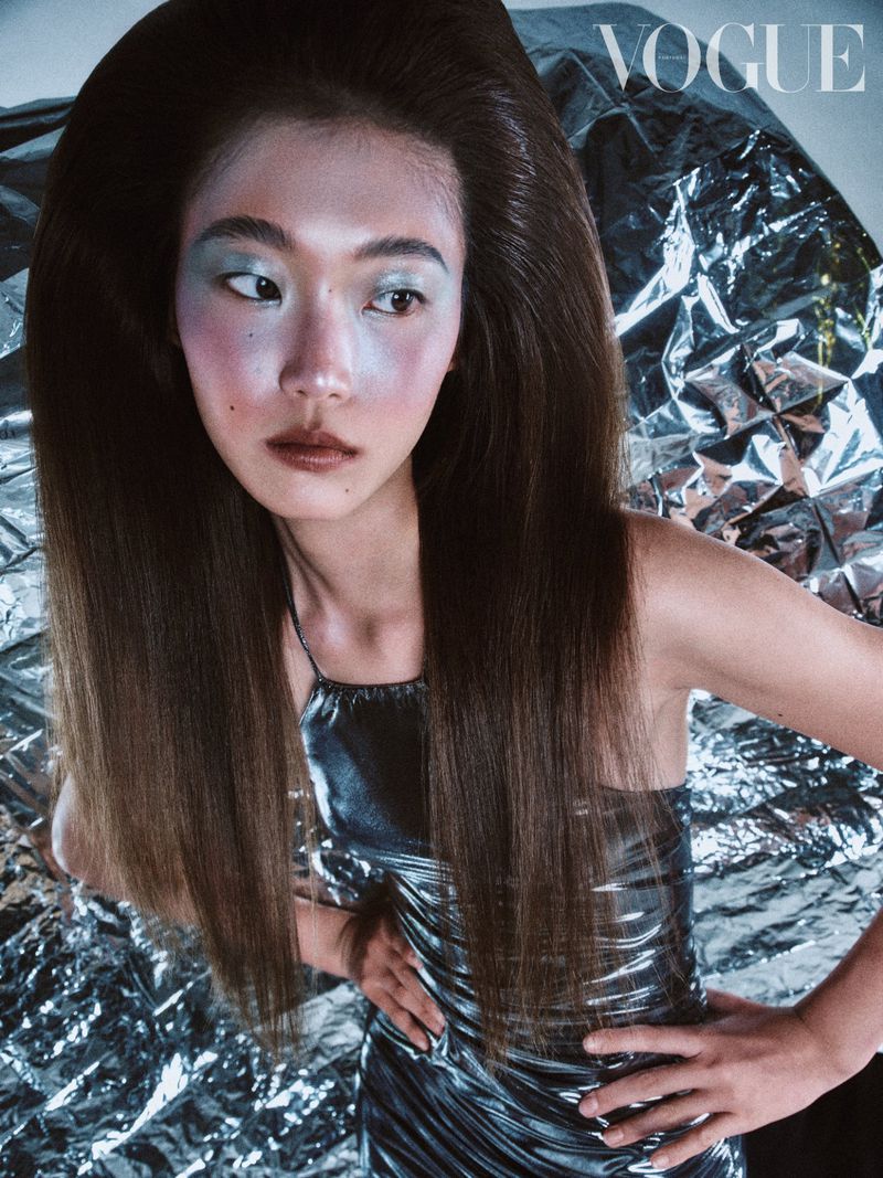 A posed Asian woman with a silver dress and long brown hair against a crumpled silver background for a Vogue magazine cover.