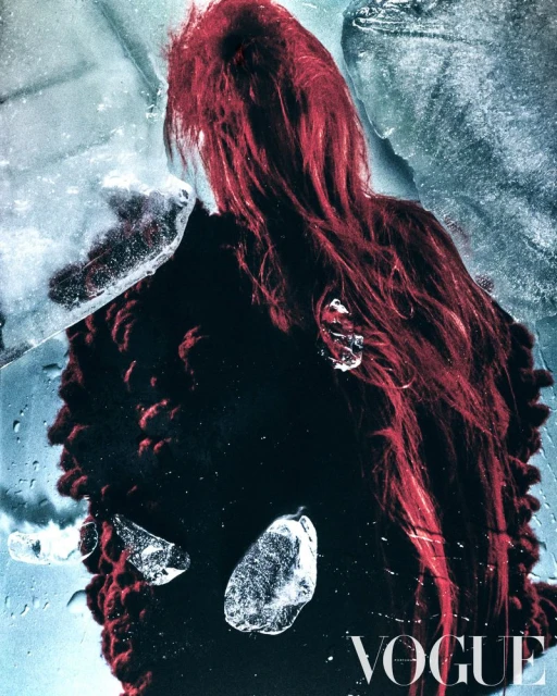 Fashion editorial shot features a person with red hair in a fuzzy black coat, ice shards, and Vogue magazine logo. Moody, cool-toned image.