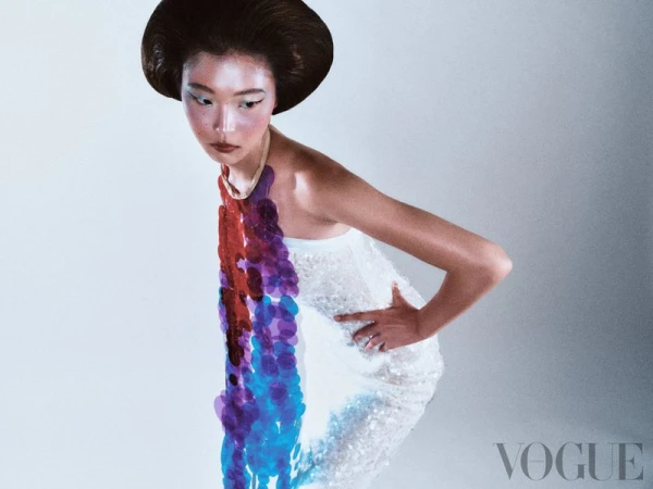 Fashion editorial portrait of an Asian woman with stylized hair and makeup, wearing a white beaded dress and statement purple necklace.