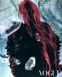 Back view of a person with long vibrant red hair wearing a dark textured knit coat behind cracked blocks of ice.