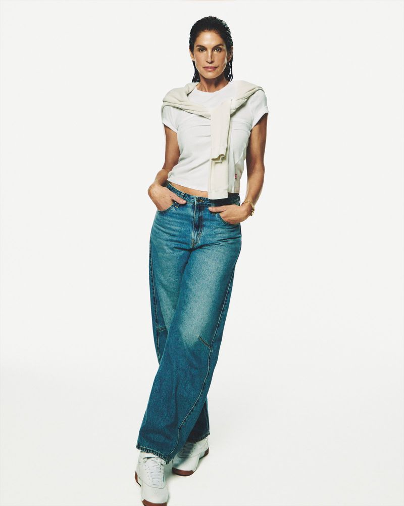 Full-length shot of an adult female in a white T-shirt and blue jeans, posing against a clean, bright white backdrop in a fashion setting.