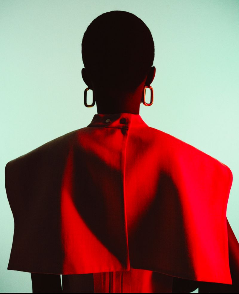 Rear view of a model in a vibrant red top with prominent earrings against a pale teal studio backdrop