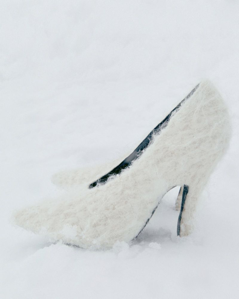 Elegant cream-colored high heel shoes sitting in a bed of snow, with a soft, dreamy aesthetic and wintery outdoor environment.